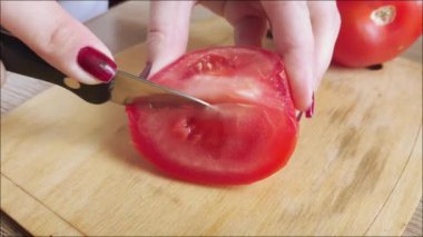 Kadın eli, mutfak masasındaki tahtalara bıçakla sulu kırmızı bir domates kesti. Taze salata pişiriyorum. Domates sosu pişirme kavramı. İtüzümü sebzeleri.