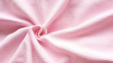 Pembe waffle kumaşı spiral şeklinde bükülmüş ve sağ tarafta yazı için bir yer var. Kumaşın, atölyenin promosyon fotoğrafı. Yumuşak pembe tekstil arkaplanı.