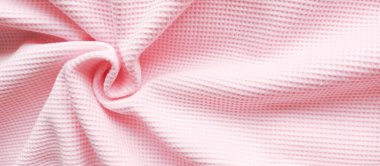 Pembe waffle kumaşı spiral şeklinde bükülmüş ve sağ tarafta yazı için bir yer var. Kumaşın, atölyenin promosyon fotoğrafı. Yumuşak pembe tekstil arkaplanı.