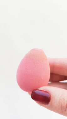 Beyaz bir arka planda bir kadının elinde temelle boyanmış pembe bir sünger, yazı için bir yer. Deriye temel uygulanıyor.