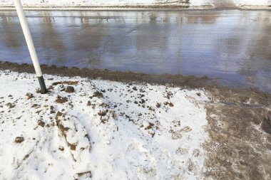 Asfalt yol boyunca kirli kar. Karda siyah is var. Otobanda su birikintileri. Çevre kirliliğinden kaynaklanan çevresel kirlilik emisyonlarla. 