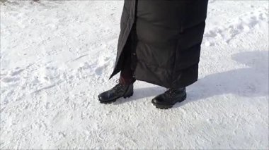 Siyah çizmeli ve uzun ceketli bir kadın karda yürüyor. Kışlık ayakkabılı ayaklar karlı bir patika boyunca yürür. Şehirdeki asfaltsız yollar kavramı. Kar yağışı sonrası yolların saldırmazlığı.
