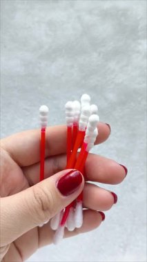 Gri arka planda, bir kadının elindeki plastik kullan-at pamuklu çubuklar. Kulakları temizlemek için pamuklu bez.. 