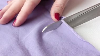Bir kadının eli makasla masanın mor kumaş astarını keser. Dişi bir terzi dikiş dikmek için belli bir kalıba göre dikiş diker. Stüdyo. Tekstil üretimi.