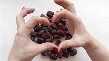 Kalp şeklinde bir kadın eli, arka planda dağınık hurmalar, eller tarihleri alır ve masaya döker. Doğal Arapça tarihler. 