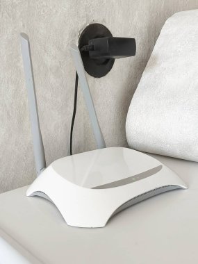 New white Wi-Fi router near potted plant on black shelf