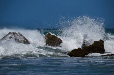 Denizin dalgaları kayalara çarpıyor, güzel ve vahşi bir koyda..