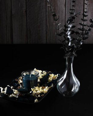 Still life of dark photo of candle and vase with black plant. clipart