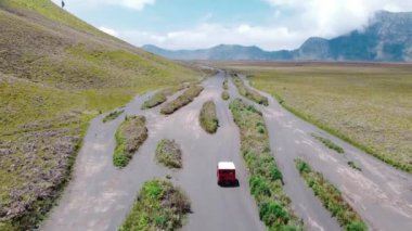 Yeşil bozkırdan geçerek dağ zirvesine doğru giden kırmızı bir off-road aracının havadan görüntüsü. Offroad aracıyla keşif..