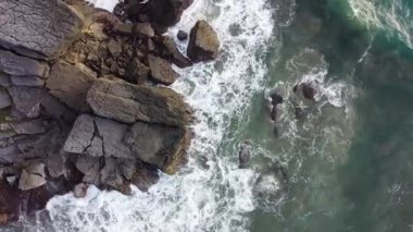 Deniz kıyısındaki kayaların drone kamerası, güzel deniz yüzeyi, kayaların üzerine çarpan inanılmaz deniz dalgaları..