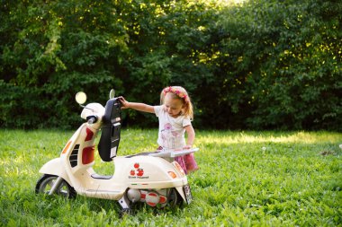 Küçük kız parkta beyaz bir scooter 'da oturuyor, yaz zamanı.