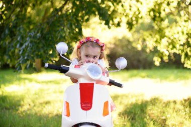 Güneşli bir günde parkta scooter süren sevimli küçük bir kız.
