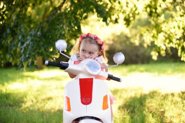 Güneşli bir günde parkta scooter süren sevimli küçük bir kız.