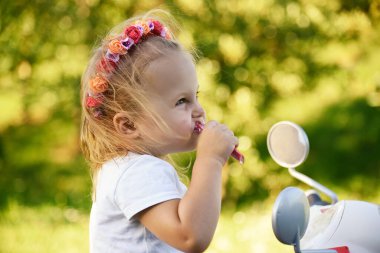 Güneşli bir günde parkta scooter süren sevimli küçük bir kız.