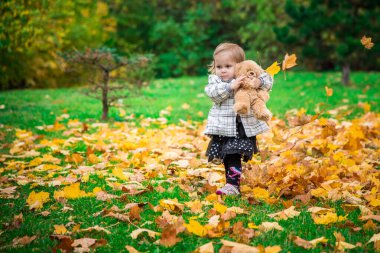 Güz parkında oyuncak ayısıyla oynayan sevimli küçük kız.