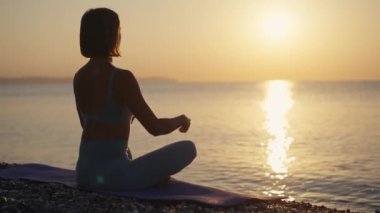 Kadın, plajda yoga pozunda meditasyon yapıyor. Yoga konsepti. El kadını sahilde nilüfer poz pratiği yapıyor.