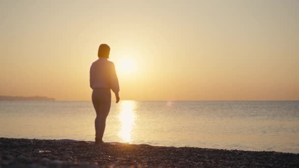 Silhouette女性は夏休みのビーチの幸福とリラクゼーションで瞑想にヨガのポーズを練習します 日没の黄金の時間とヨガ瞑想の海のビーチで穏やかな女性の運動 精神衛生 — ストック動画