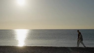 Olgun çift gün doğumunda sahilde sörfe doğru yürür.