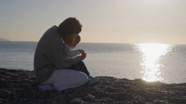 Anne deniz atında bebekle oynuyor, güzel bir gün doğumu, küçük çocuğu kucaklayan bir kadın, anne-baba sevgisi, denizin üzerinde parlayan güneş. Yüksek kalite 4k görüntü