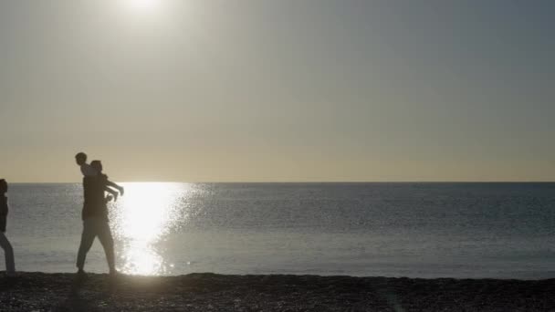 美しい夕日を見ている子供を持つ若い家族 子は海の近くで遊んでいます 健康的なライフスタイルのコンセプト — ストック動画