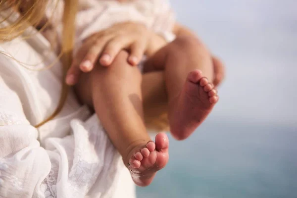 Bare feet of a cute newborn baby in warm white clothes at the sea. Childhood. Small bare feet of a little baby girl or boy. Sleeping newborn child. High quality photo