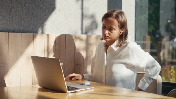 累了的女人在电脑前工作了很长时间 坐着不动 腰酸背痛很厉害 年轻女性在办公室里用笔记本电脑的时候感到头痛脚痛 — 图库视频影像