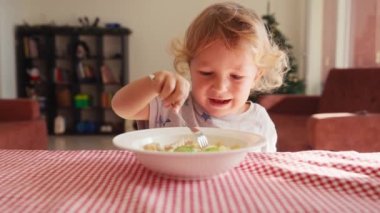 İki yaşında gülümseyen bir oğlan çocuğu sandalyeye oturur ve çatalla ketçapla makarna yer. Arka plan bulanık. Çocuklar için sağlıklı beslenme. Childs beslenme. 