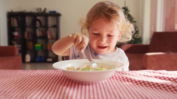 两岁的小男孩笑着坐在高椅子的桌旁 用番茄酱和叉子从碗里吃着意大利面 模糊的背景 孩子们的健康饮食 儿童营养 — 图库视频影像