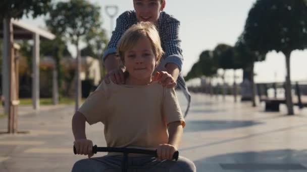 公園で子供の自転車に乗るのが楽しい白人の男の子 弟が彼を押している間 幸せな男の子はバランスバイクで楽しんでいます — ストック動画