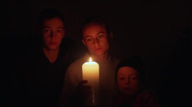 Kesinti sırasında mumların yanında iki çocuklu bir kadın bekliyor. Anne, Ukrayna 'daki enerji krizi sırasında oğullarıyla birlikte mum ışığı altında..