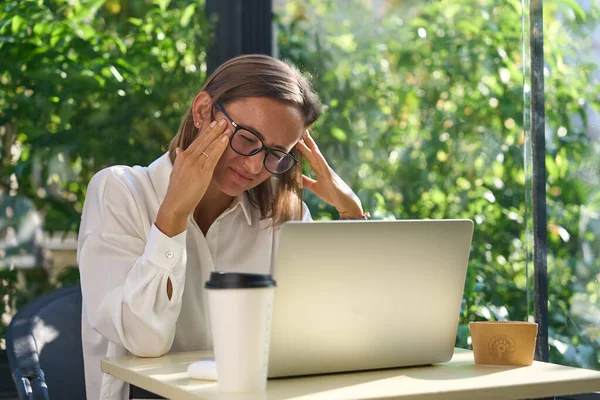 Kafkasyalı genç bir kadın migren ağrısı çekiyor. Ofiste dizüstü bilgisayarla çalışırken çok çalışan iş kadını finansörü. Yüksek kalite fotoğraf