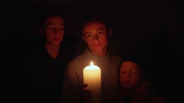 Kesinti sırasında mumların yanında iki çocuklu bir kadın bekliyor. Anne, Ukrayna 'daki enerji krizi sırasında oğullarıyla birlikte mum ışığı altında..