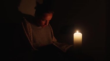 Mum ışığında kitap okuyan genç bir kadın. Elektrik kesintisi konsepti. Ukrayna 'da Savaş.