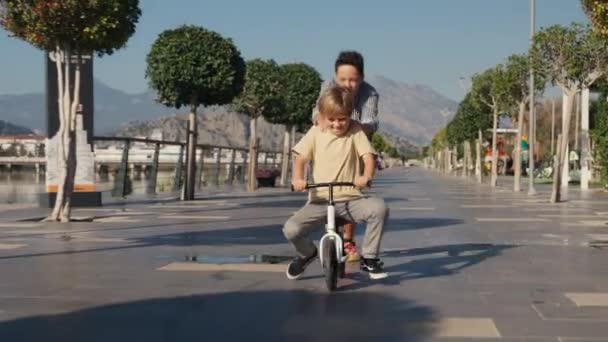 白人男孩在公园骑自行车玩得很开心 当他哥哥推他时 快乐的男孩骑自行车玩得开心极了 — 图库视频影像