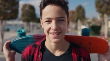 Portrait of caucasian 13 years old boy holding skateboard at sunny day