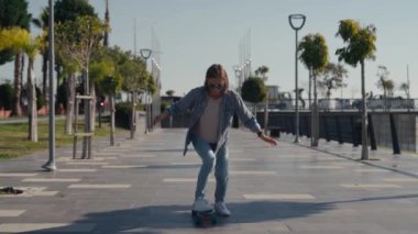 Young stylish teenage girl learning to ride skateboard. Trendy girl first time tries to ride skateboard. High quality 4k footage
