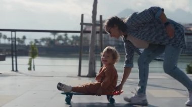 Mother pushing little son sitting on skateboard