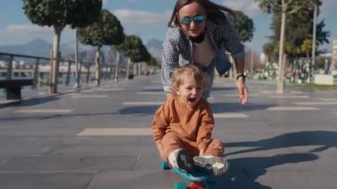Mother pushing little son sitting on skateboard