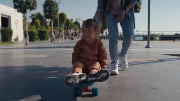 Mother Pushing Little Son Sitting Skateboard — Stockvideo