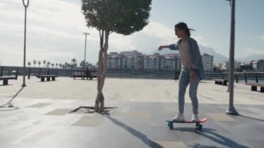 Young stylish teenage girl learning to ride skateboard. Trendy girl first time tries to ride skateboard. High quality 4k footage