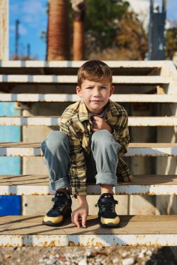 Child sitting on the steps. Portrait of handsome kid boy wearing casual sitting on the stairs on the street. Stylish boy looking at camera. Teenage boy, child outdoors in summer or spring.