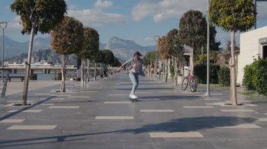 Young stylish teenage girl learning to ride skateboard. Trendy girl first time tries to ride skateboard. High quality 4k footage