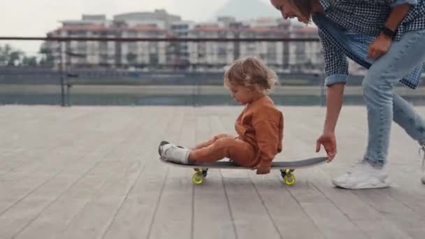 Mother Pushing Little Son Sitting Skateboard High Quality Footage — Vídeo de Stock