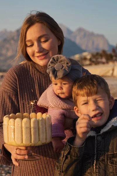 Single parent family celebrate kids bithday at sunrise on the beach with homemade cake. Single mother