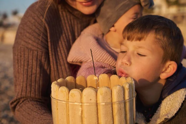 Single parent family celebrate kids bithday at sunrise on the beach with homemade cake. Single mother