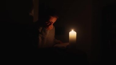 Mum ışığında kitap okuyan genç bir kadın. Elektrik kesintisi konsepti. Ukrayna 'da Savaş.