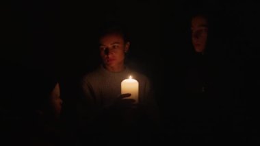 Kesinti sırasında mumların yanında iki çocuklu bir kadın bekliyor. Anne, Ukrayna 'daki enerji krizi sırasında oğullarıyla birlikte mum ışığı altında..