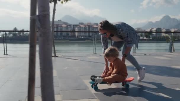 Mother Pushing Little Son Sitting Skateboard — Vídeo de Stock