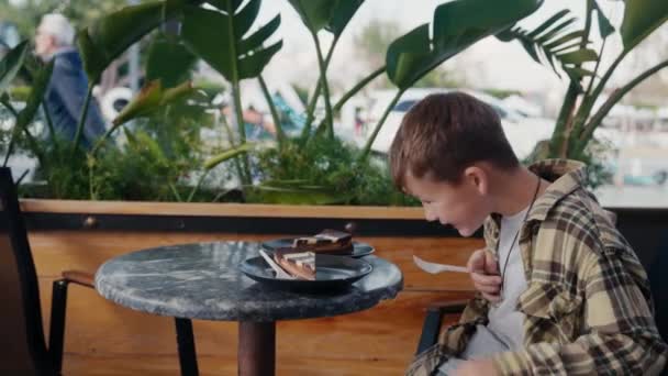 パン屋でおいしいケーキを食べている白人の子供は おいしい幸せな顔で口の中にケーキをすくっています 幸せなライフスタイル ベーカリーカフェショップ 甘いデザートフードの概念 高品質4K映像 — ストック動画