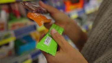 Young woman chooses protein bars in a store and reads the composition. Sport nutrition.